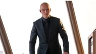 Lex Luthor stands in his office, listening through an earpiece as he prepares his next move. (Image via DC)